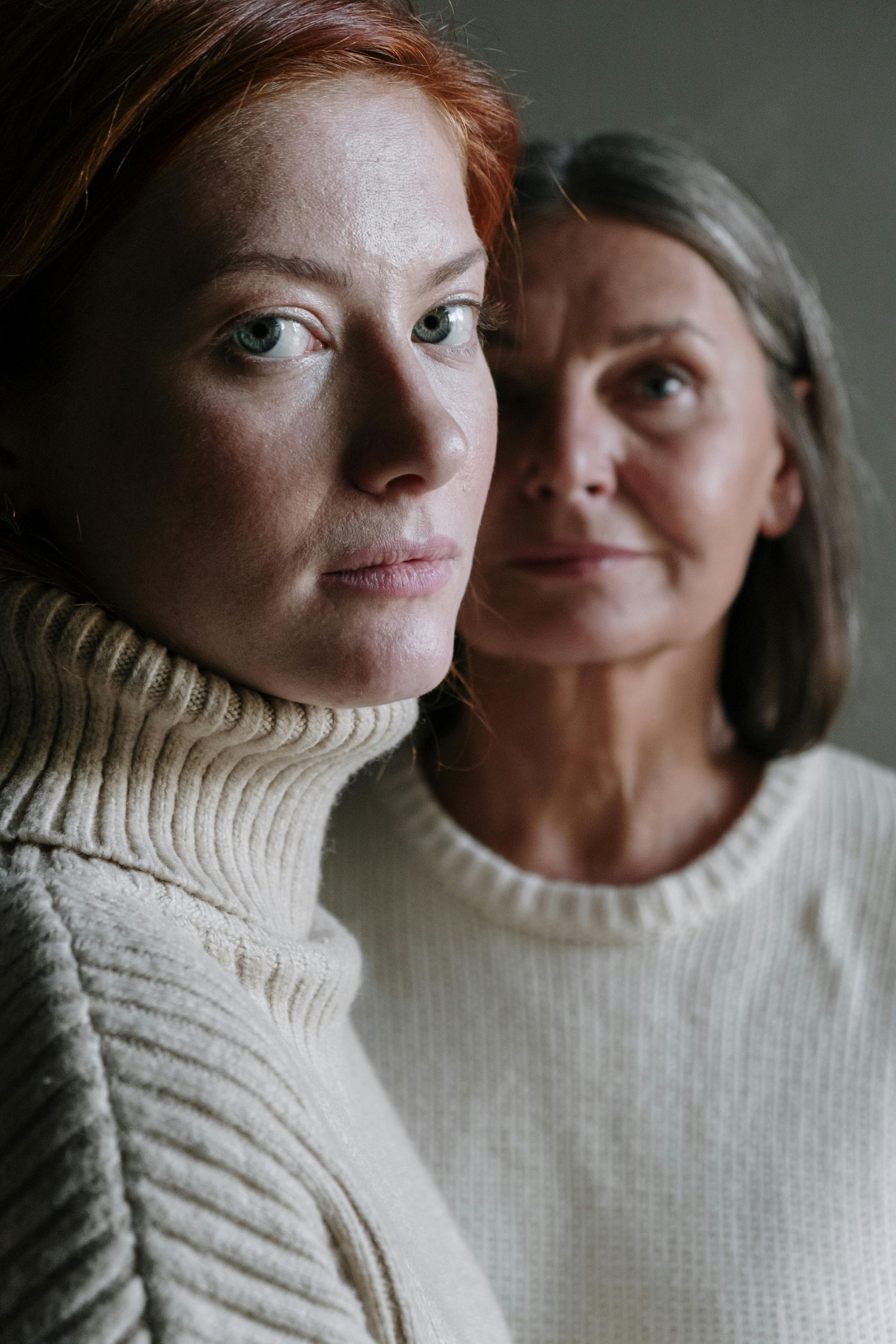 Two women in white sweaters are standing next to each other and looking at the camera.