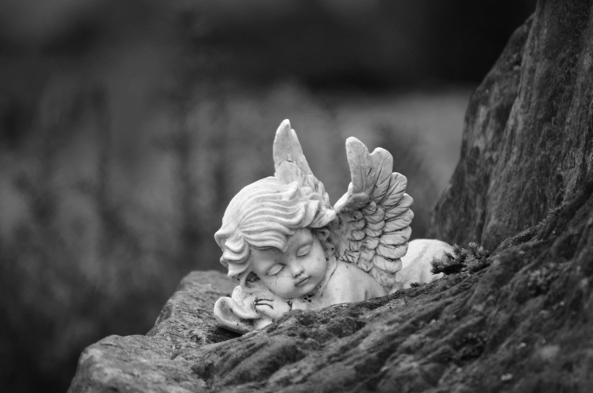 A black and white photo of a statue of an angel sleeping on a rock.