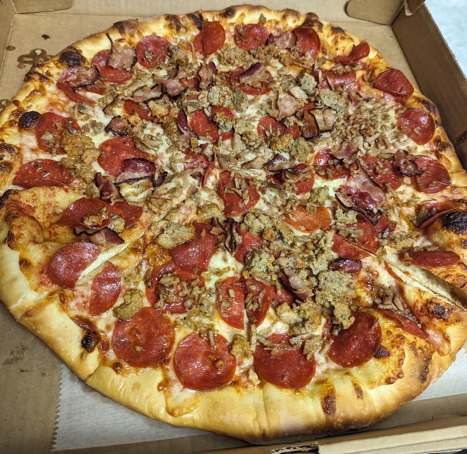 A pizza with pepperoni and sausage is in a box.