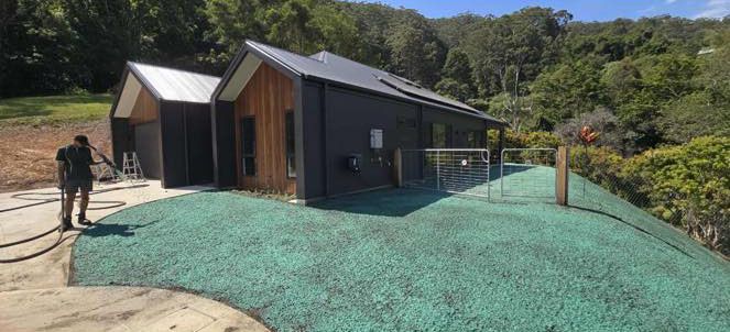 A Person Is Spraying an Artificial Turf Lawn in Front of A Modern House — East Coast Hydroseeding in Taree, NSW
