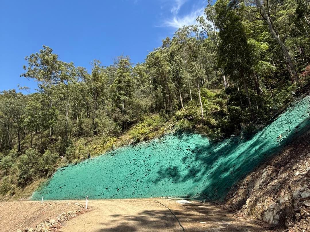 Green Erosion Control Netting Covers a Hillside Alongside a Dirt Road — East Coast Hydroseeding in Cooperabung, NSW