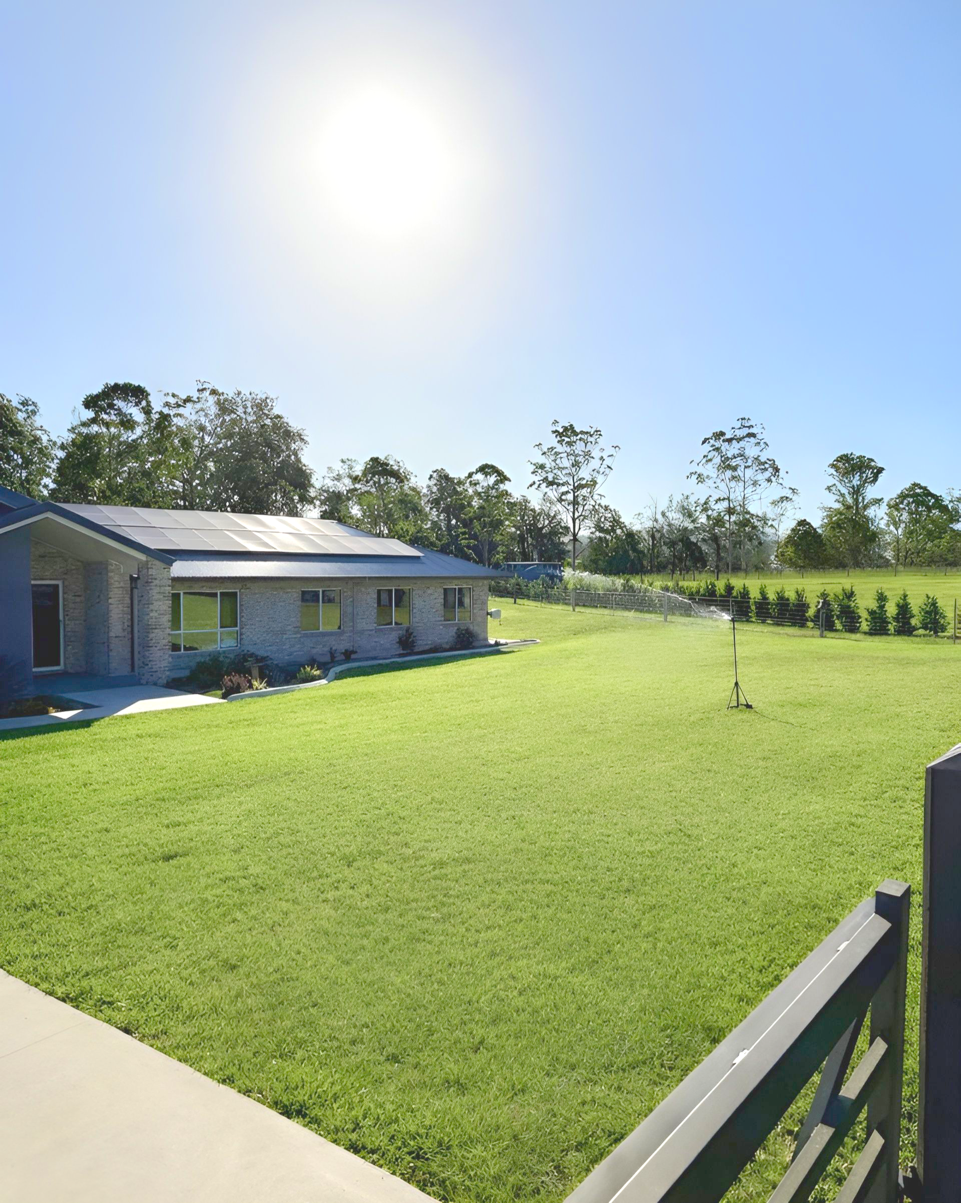 A bright, sunlit day over a stone exterior house with a green lawn and a wooden fence in the foreground — East Coast Hydroseeding in Cooperabung, NSW