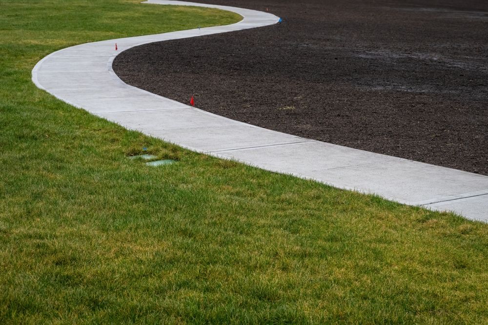 Curving Concrete Sidewalk Separating Green Grass from Dark, Gravel-Covered Area — East Coast Hydroseeding in Wauchope, NSW