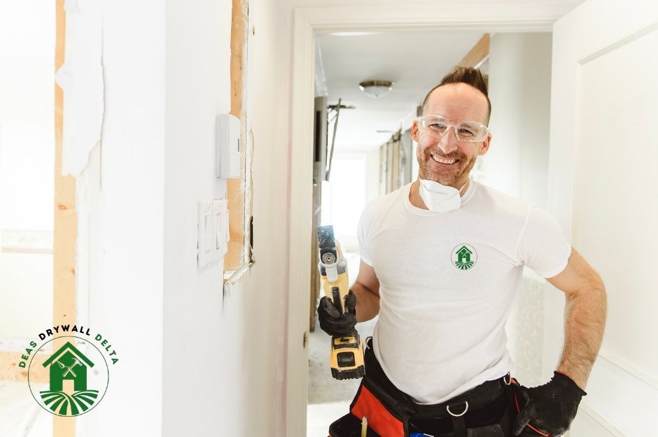 A drywall repair company professional in a white polo shirt, standing in a bright hallway, holding a yellow cordless power drill. Commercial construction materials visible in the background near Laurier Ave, and Granville St, Vancouver, BC.