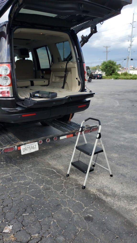 A ladder is attached to the back of a car in a parking lot.