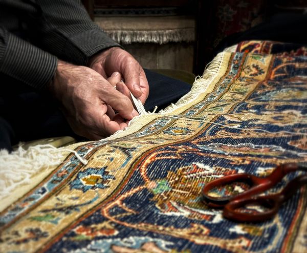 Hands with a needle and thread work on fabric.