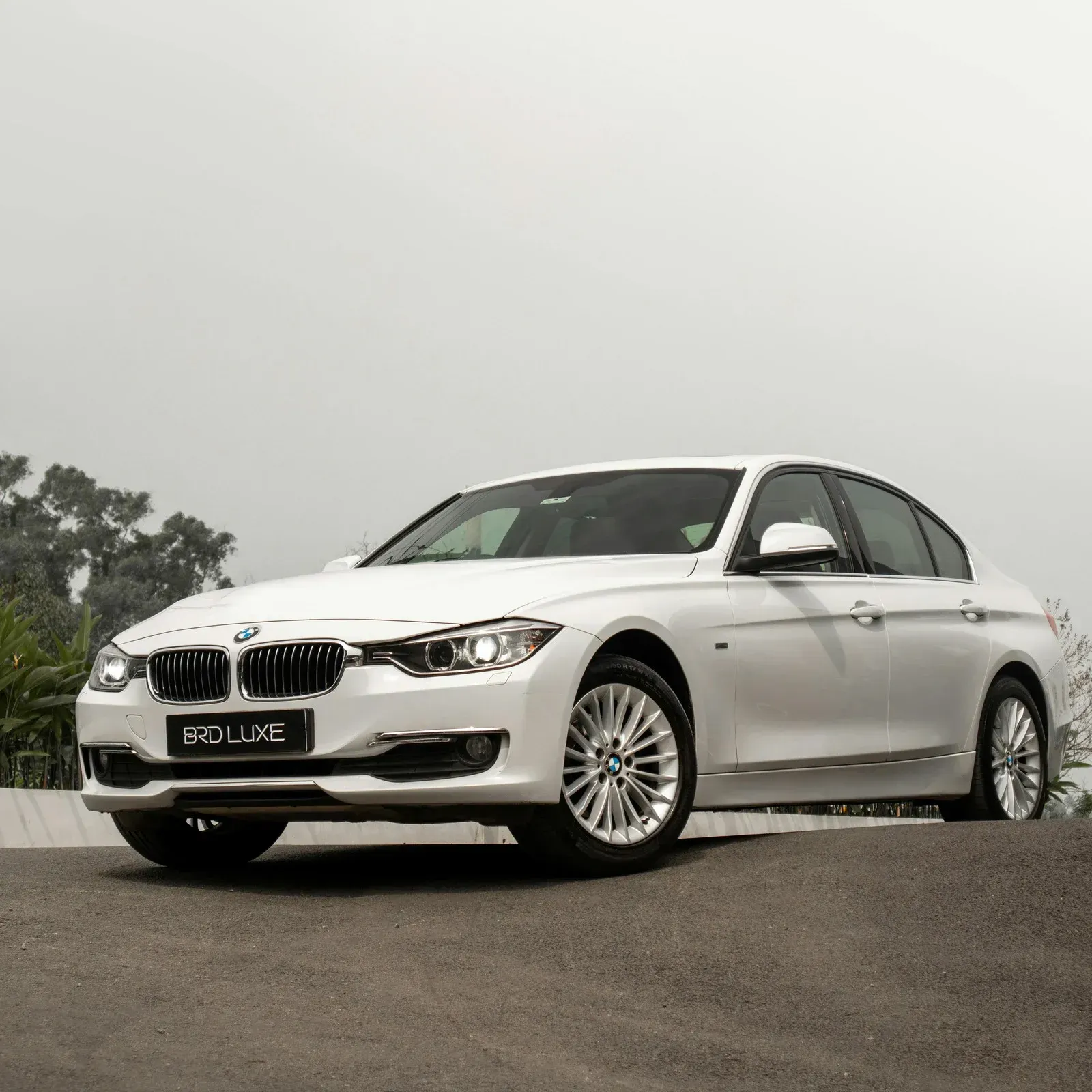 White BMW sedan parked on a paved area, trees in the background, cloudy sky.