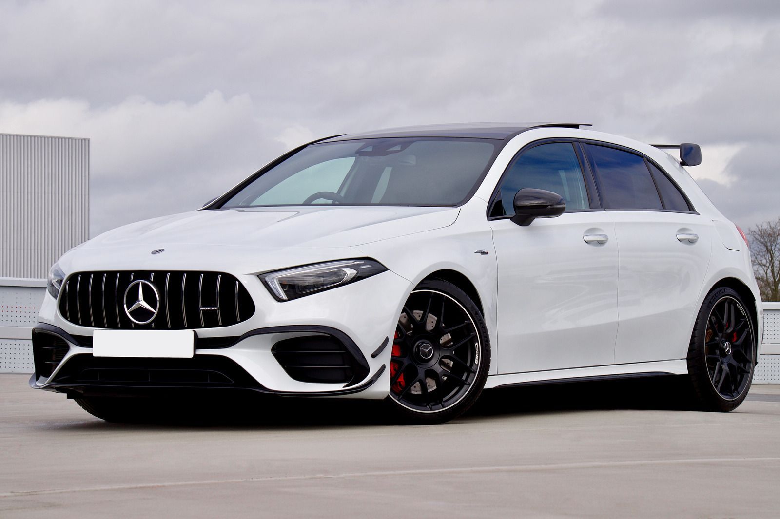 White Mercedes-AMG A-Class hatchback parked on a rooftop. Black grille, wheels, and spoiler.