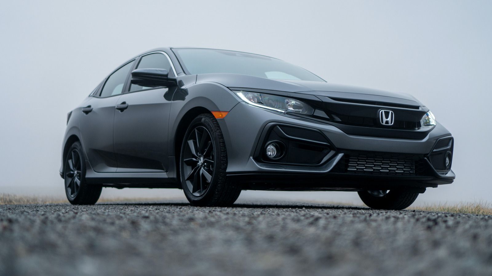 Gray Honda Civic hatchback on a gravel road in a foggy setting, black wheels.