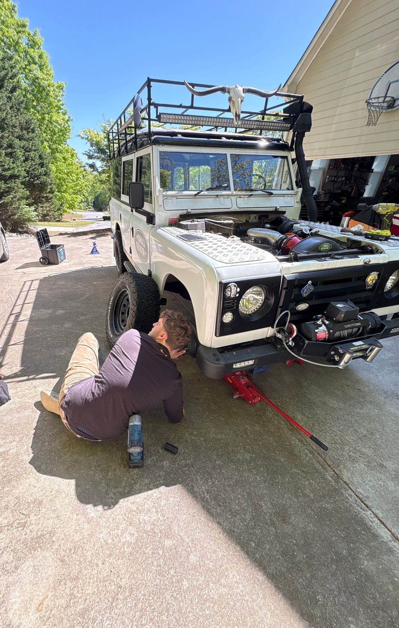 Man working on white Land Rover SUV outdoors, sunny day.