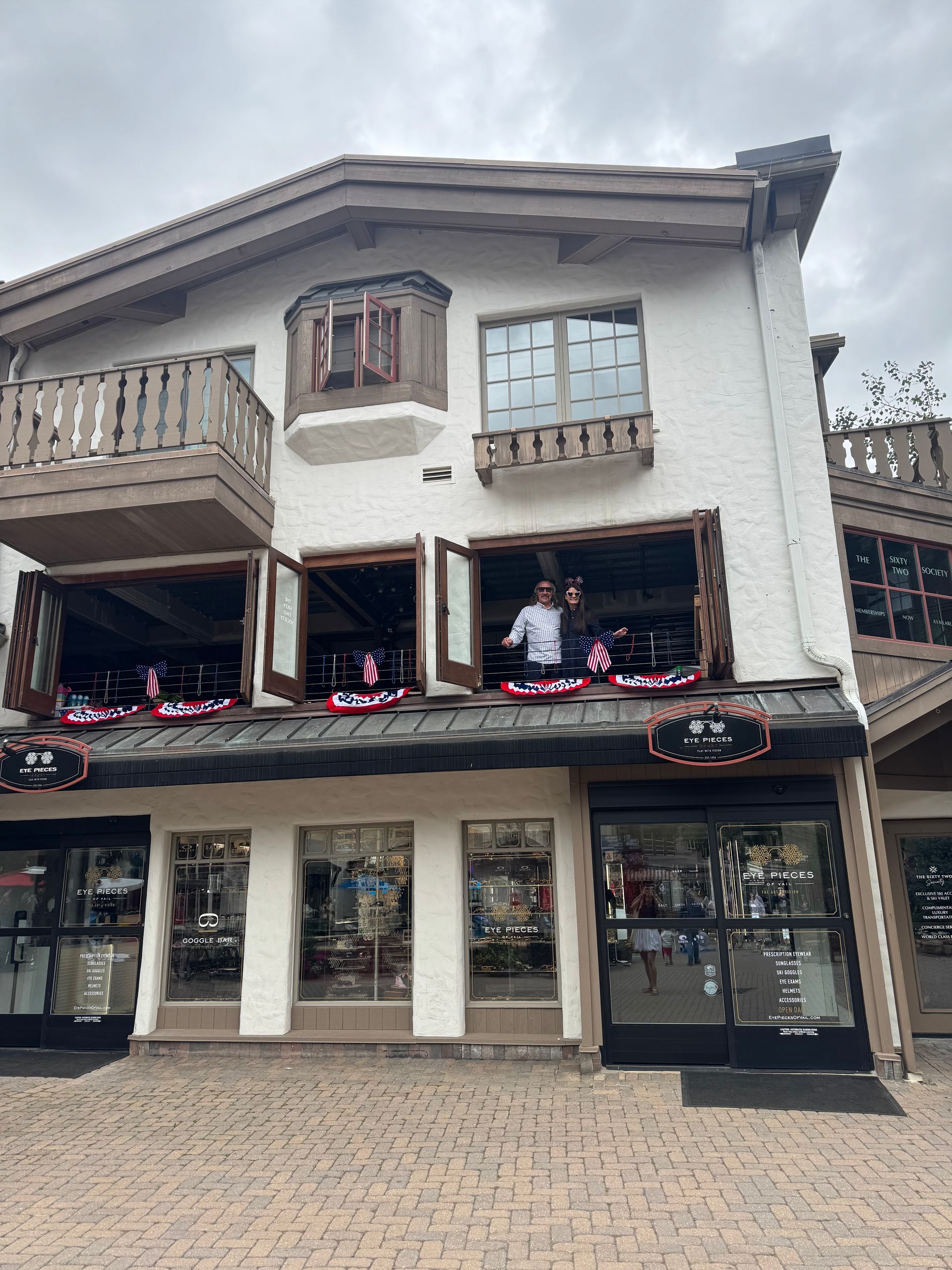 Two-story building with open windows, people visible, and shops below a cloudy sky.
