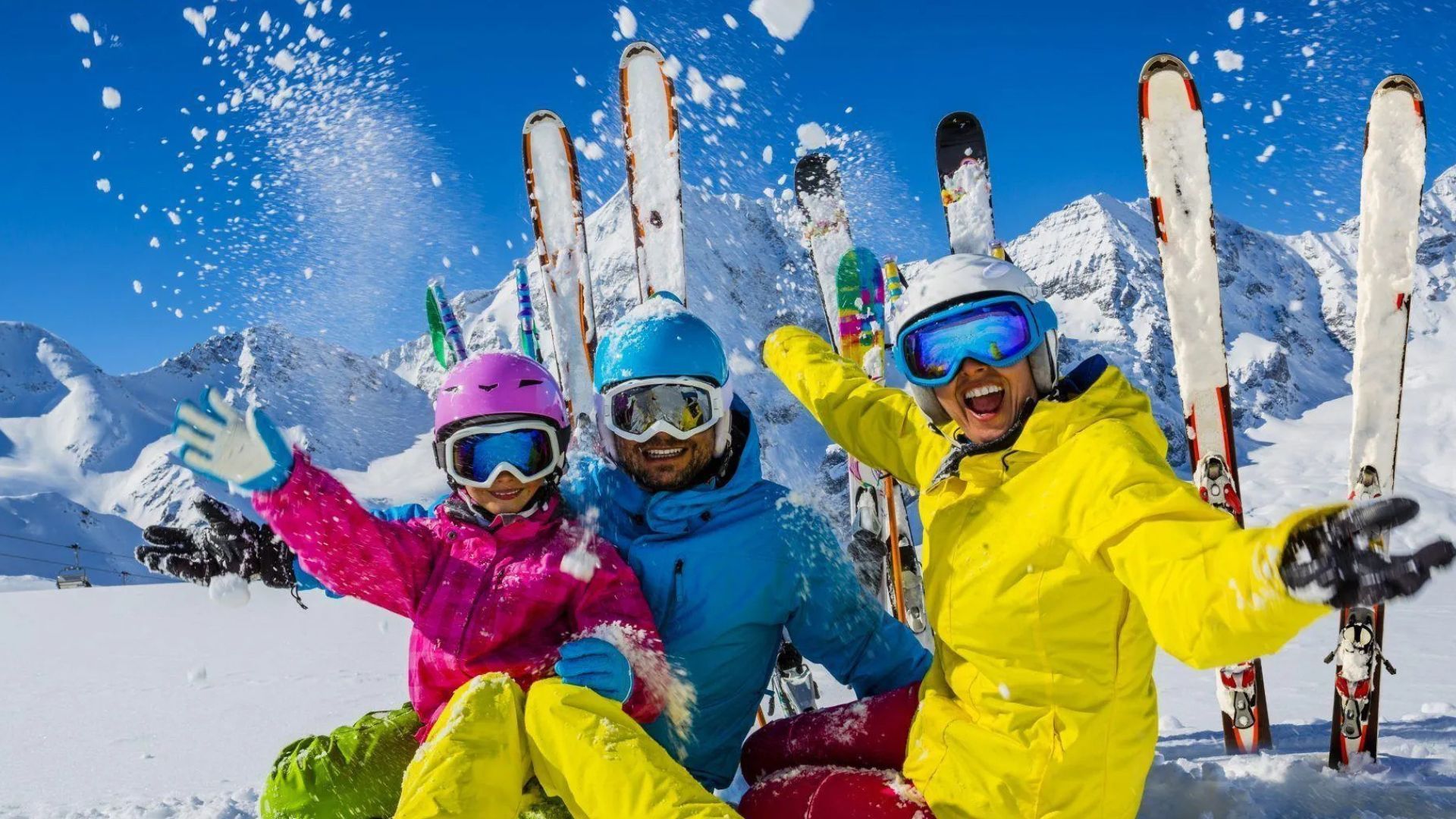 A family laughing and enjoying a ski day on a snowy mountain with a blue sky