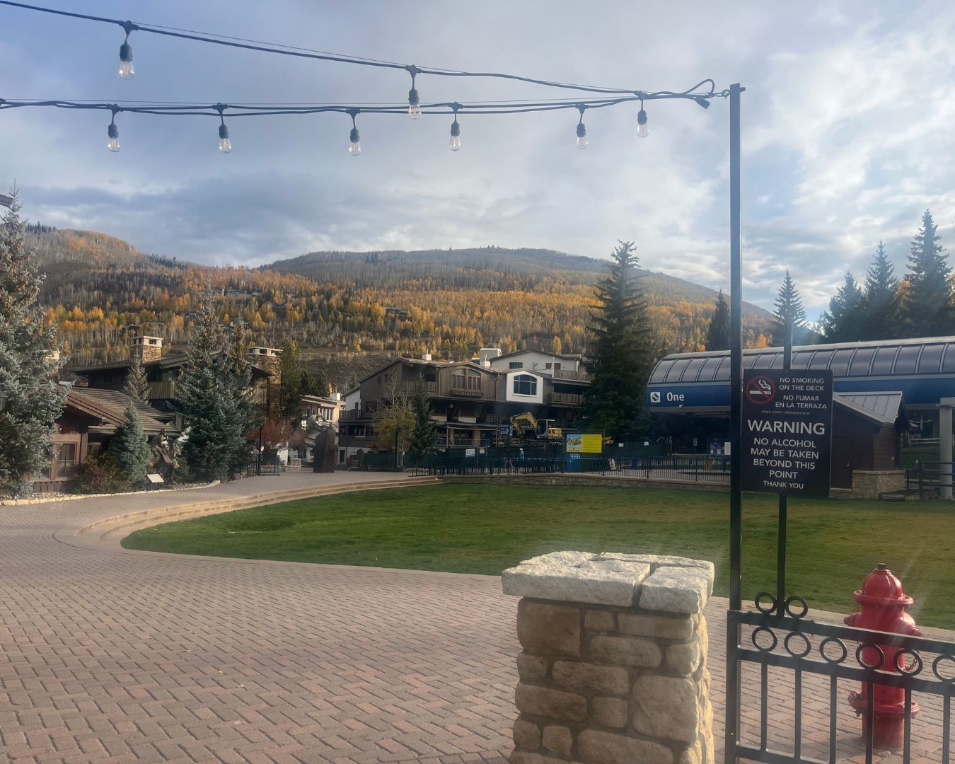 Brick plaza with a grassy area and shops in a mountain town setting; a red fire hydrant is visible.