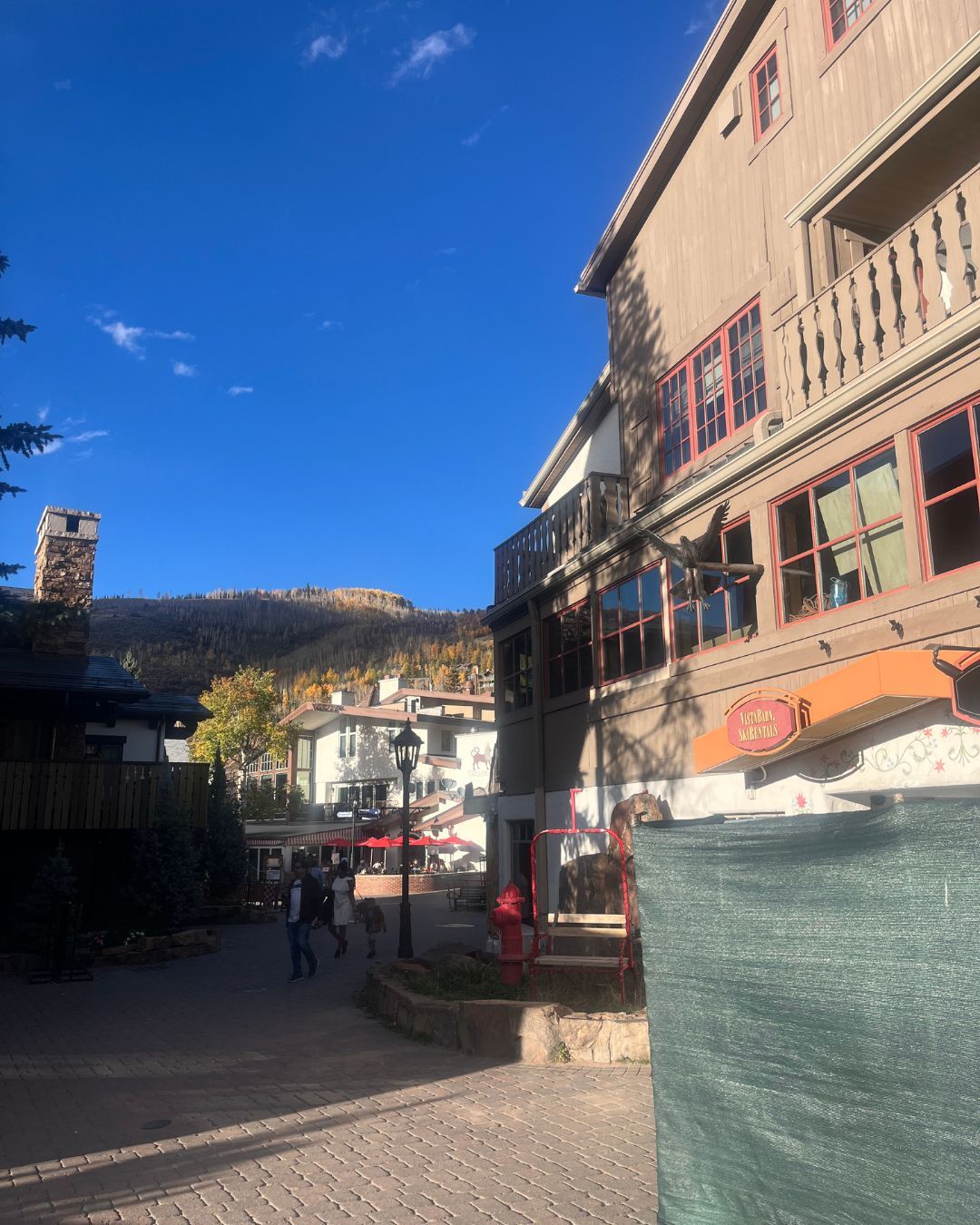 Buildings line a street on a sunny day with blue sky and a mountain in the distance.