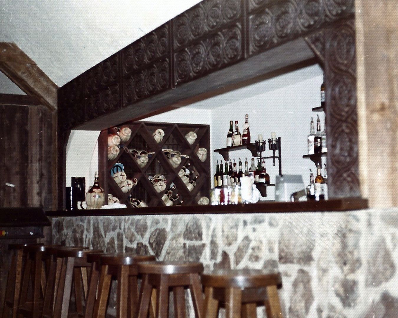Bar interior with stone facade, wooden stools, and shelves of liquor bottles.