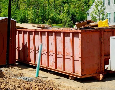 Red construction dumpster filled with debris, outdoors.