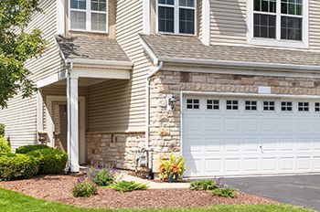 Tan and stone facade home with a white garage door and green landscaping.