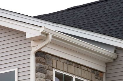 White gutters and trim on a house with grey siding, stone accents, and a dark roof.