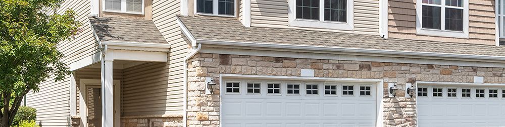 Exterior view of a multi-story home with white garage doors and stone detailing.