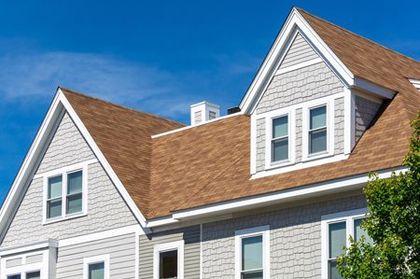 House with brown roof, white trim, gray siding, and blue sky.