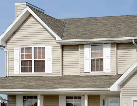 Two-story beige house with white trim, windows, and roof, under a blue sky.