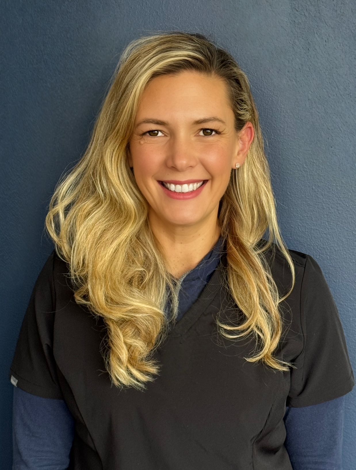 A woman with blond hair wearing scrubs and smiling for the camera