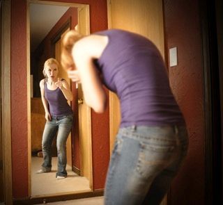 A woman in a purple tank top is standing in front of a mirror