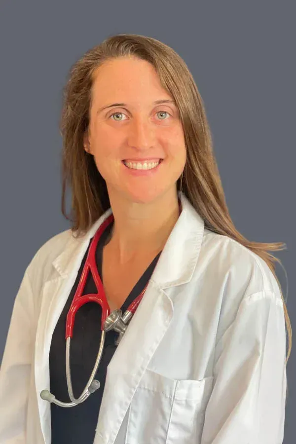 A woman in a lab coat with a stethoscope around her neck is smiling.