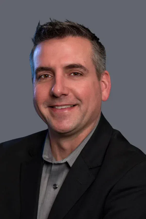 A man in a suit and gray shirt is smiling for the camera.