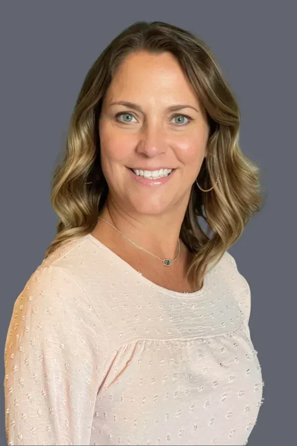 A woman in a pink shirt is smiling for the camera.