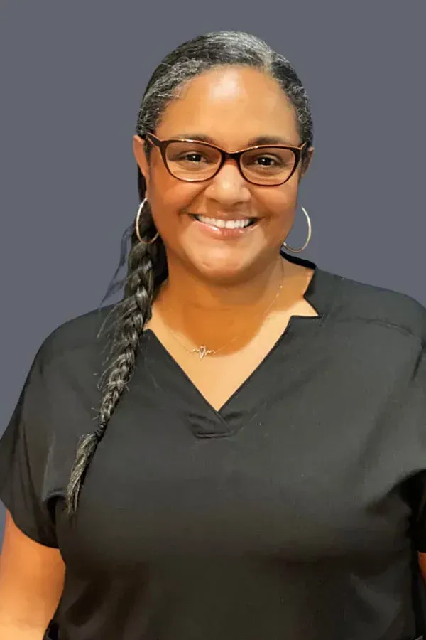 A woman wearing glasses and a black scrub top is smiling for the camera.