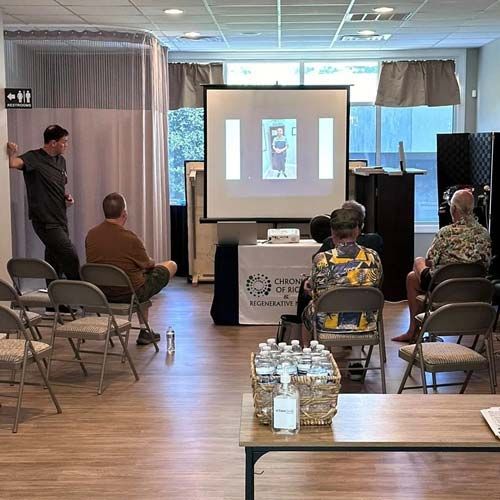 A group of people are sitting in chairs in front of a projector screen.