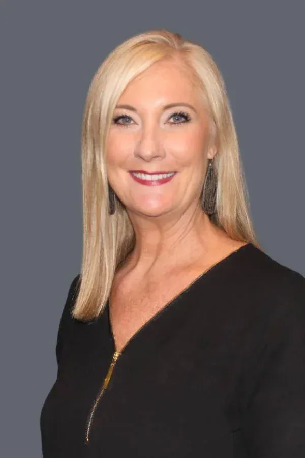 A woman with blonde hair is wearing a black shirt and smiling for the camera.