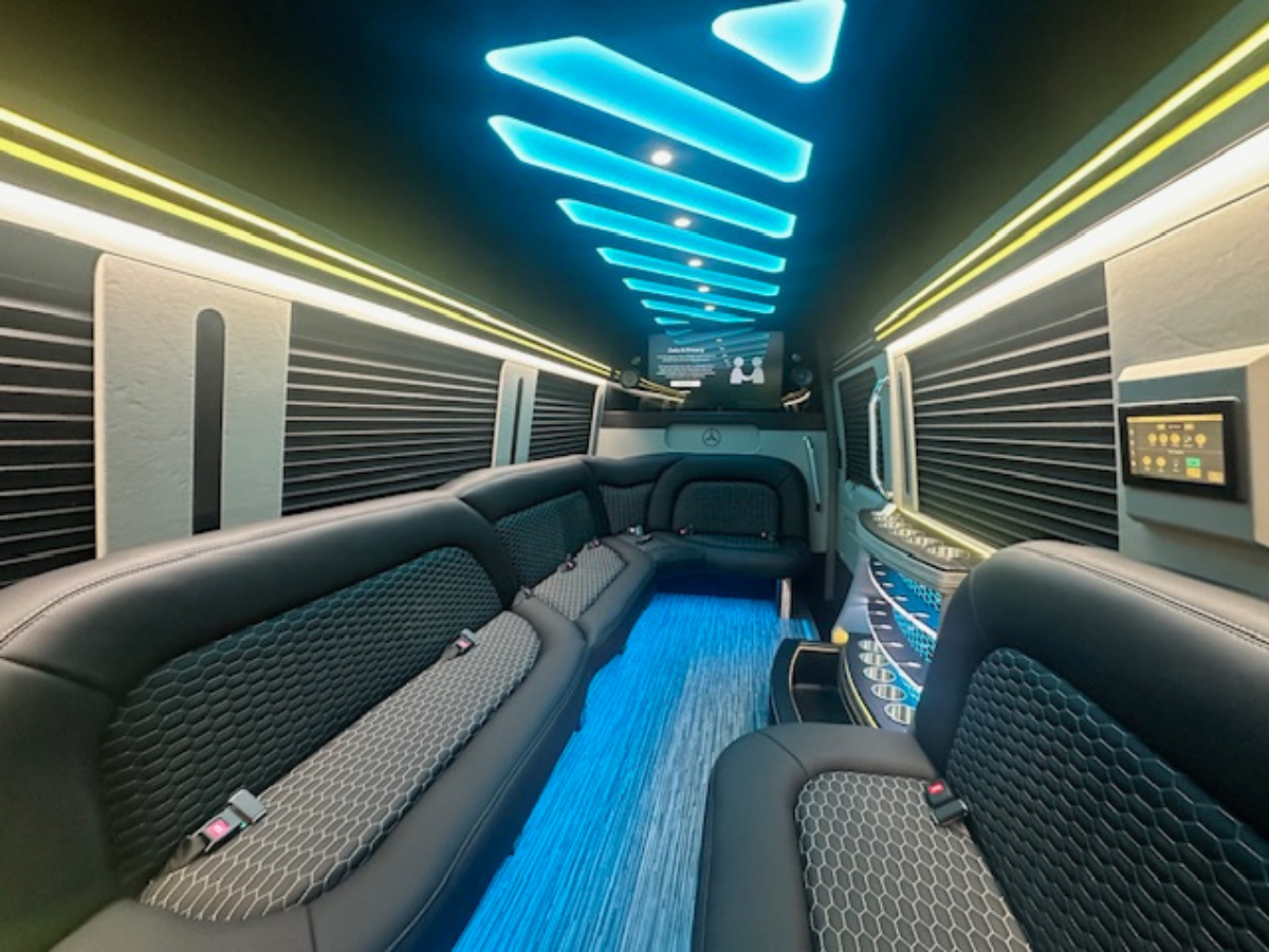 Interior of a luxury van with blue LED lighting on the ceiling and floor, black leather seating.