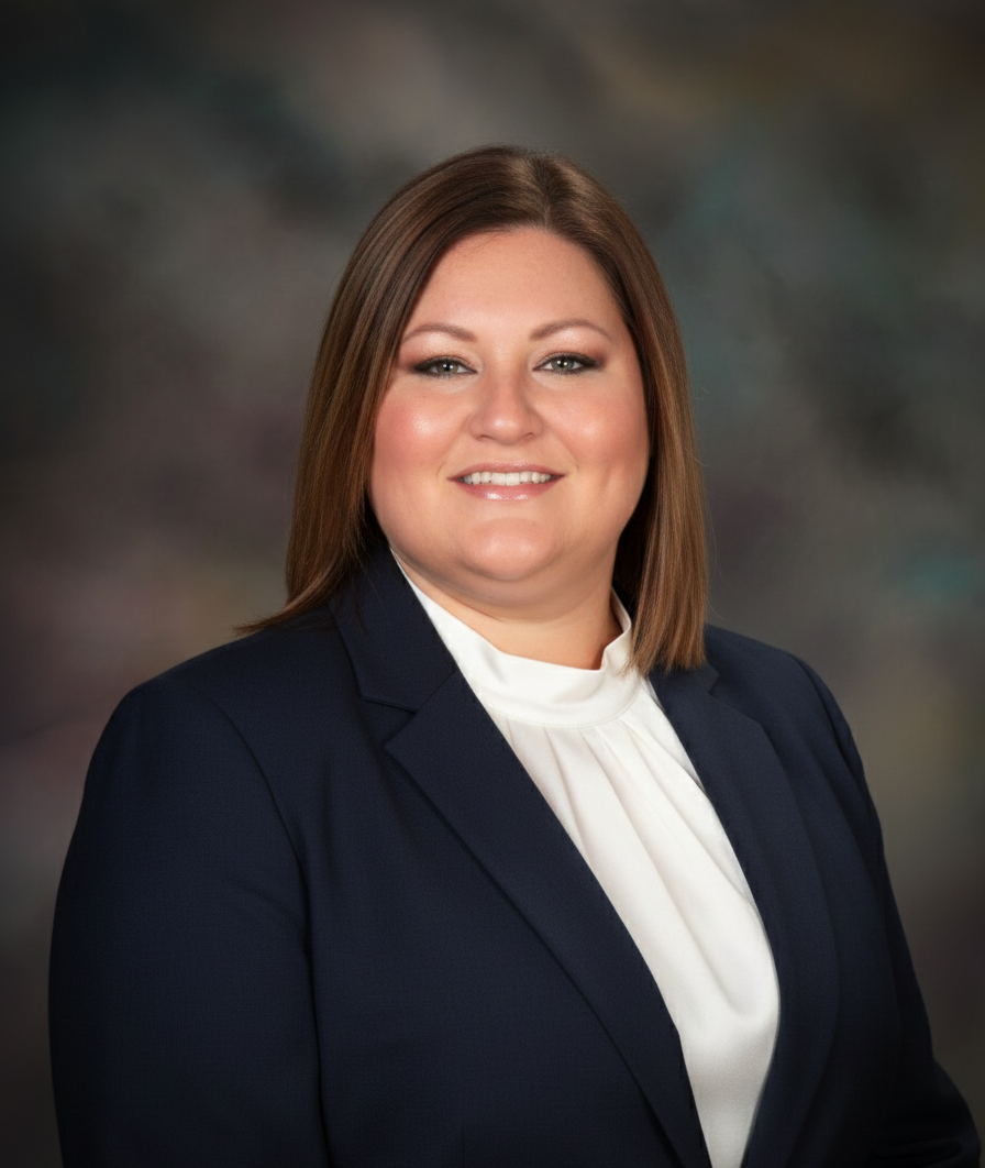 Woman smiling, wearing a navy blazer over a white blouse, against a blurred background.