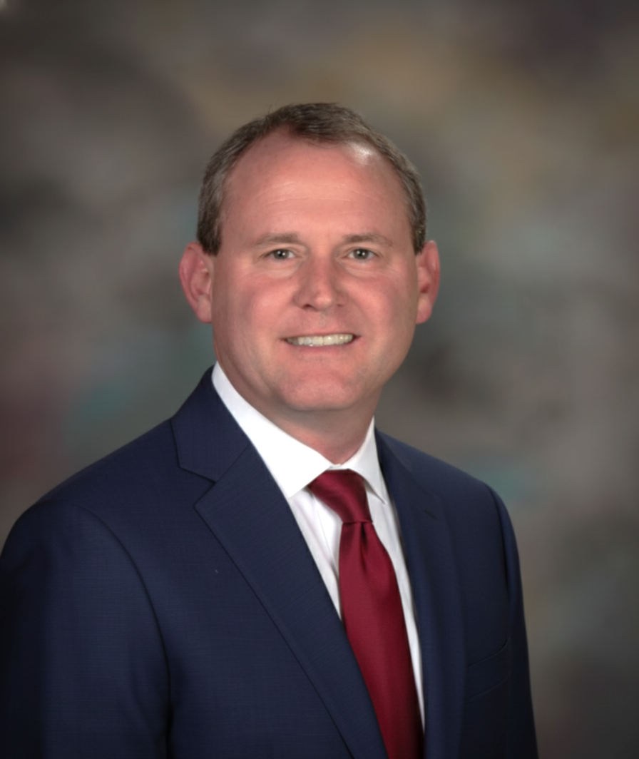 Man in blue suit, red tie, smiling at camera against blurred backdrop.