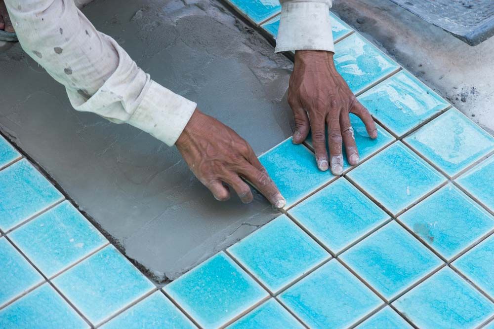 A Man is Laying Tiles on the Floor of a Swimming Pool — All Over Pool Removals in Surrey Hills, VIC