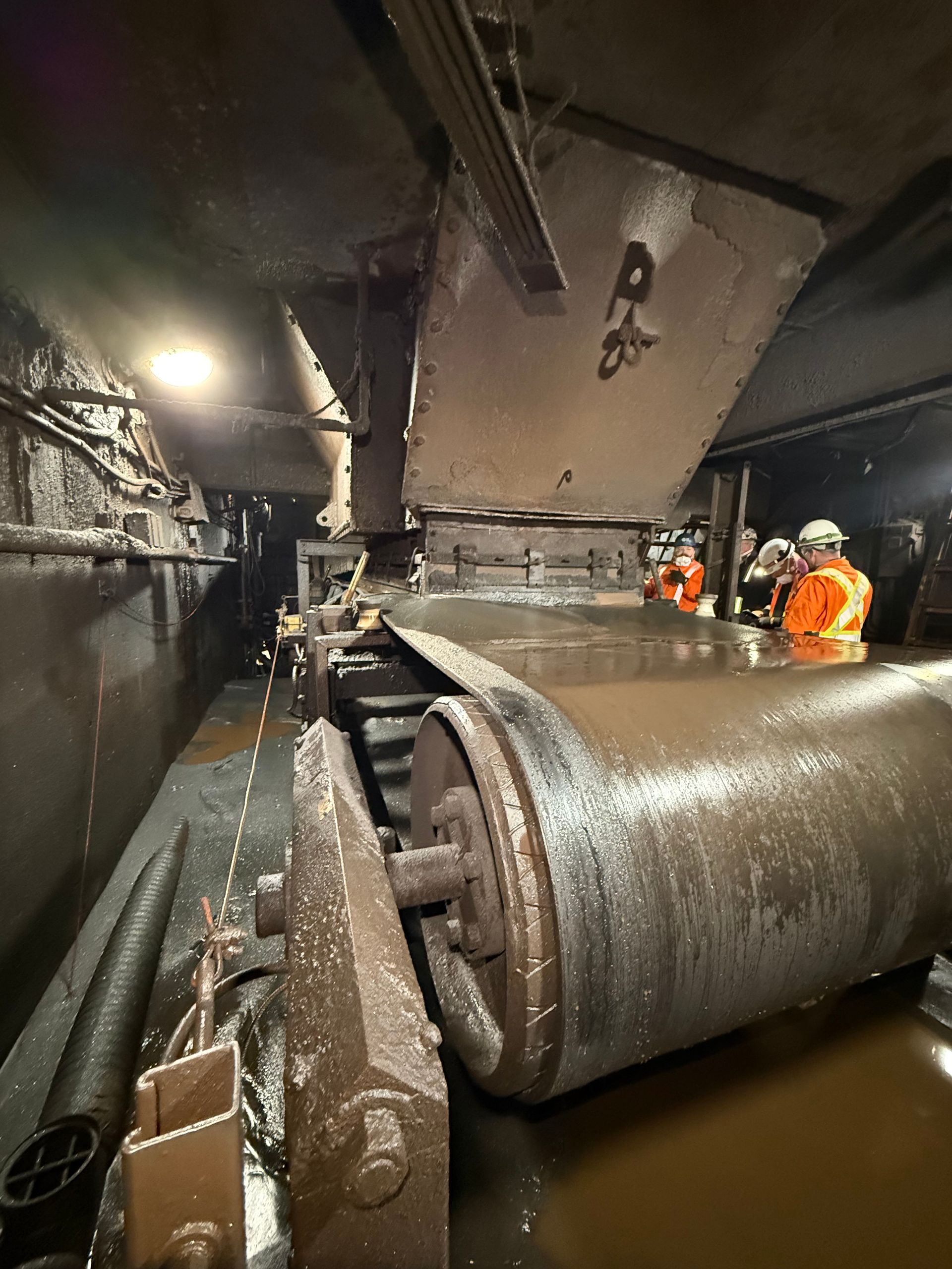 Travaux d'entretien de canalisations industrielles dans un tunnel inondé : des ouvriers en tenue de sécurité orange inspectent une grosse canalisation métallique.