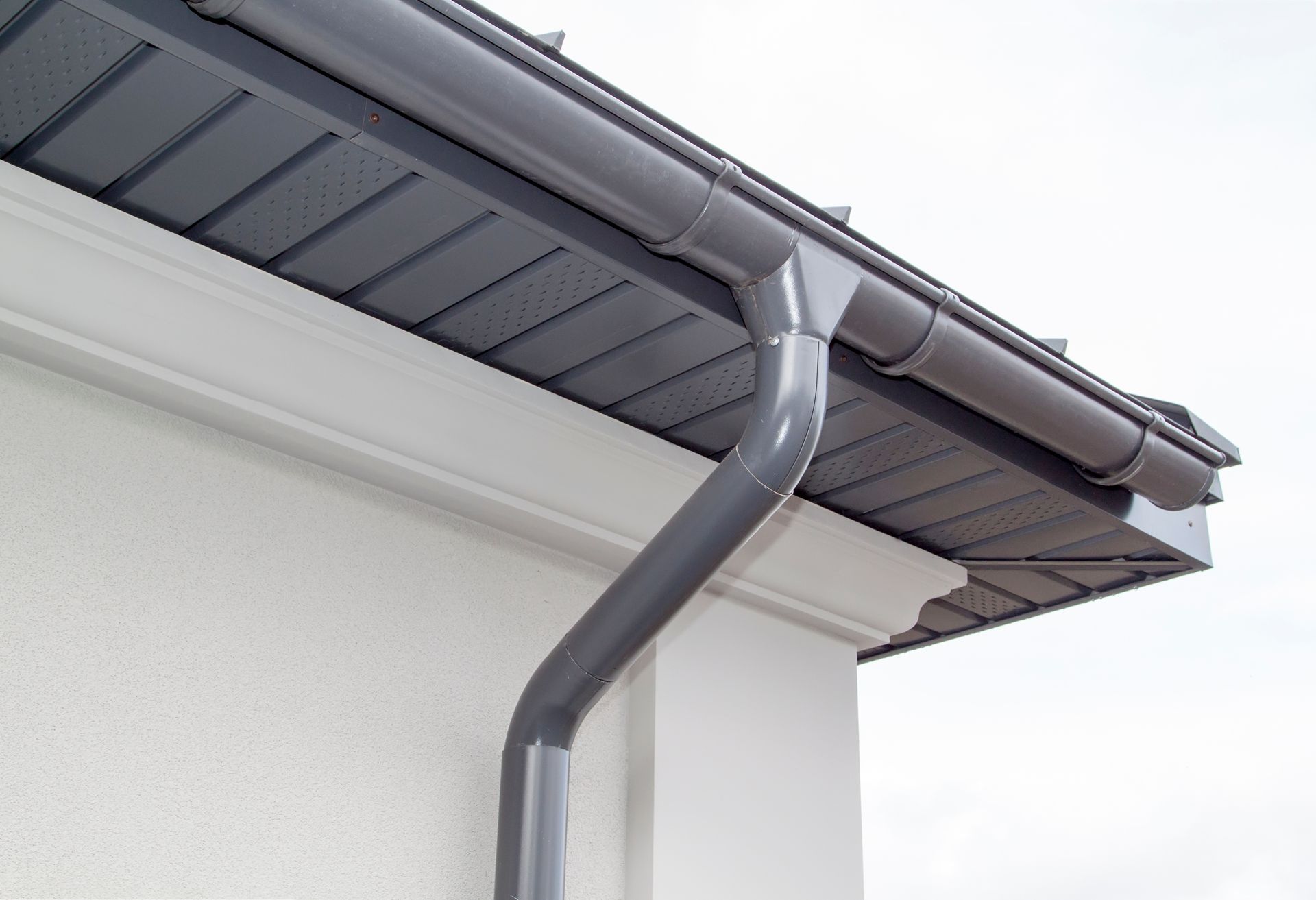 Gray metal rain gutter and downspout on modern residential home roof and fascia.