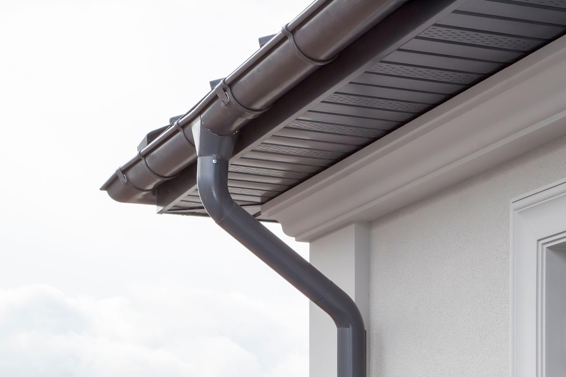 Gray seamless gutter and downspout installed on a residential roofline.