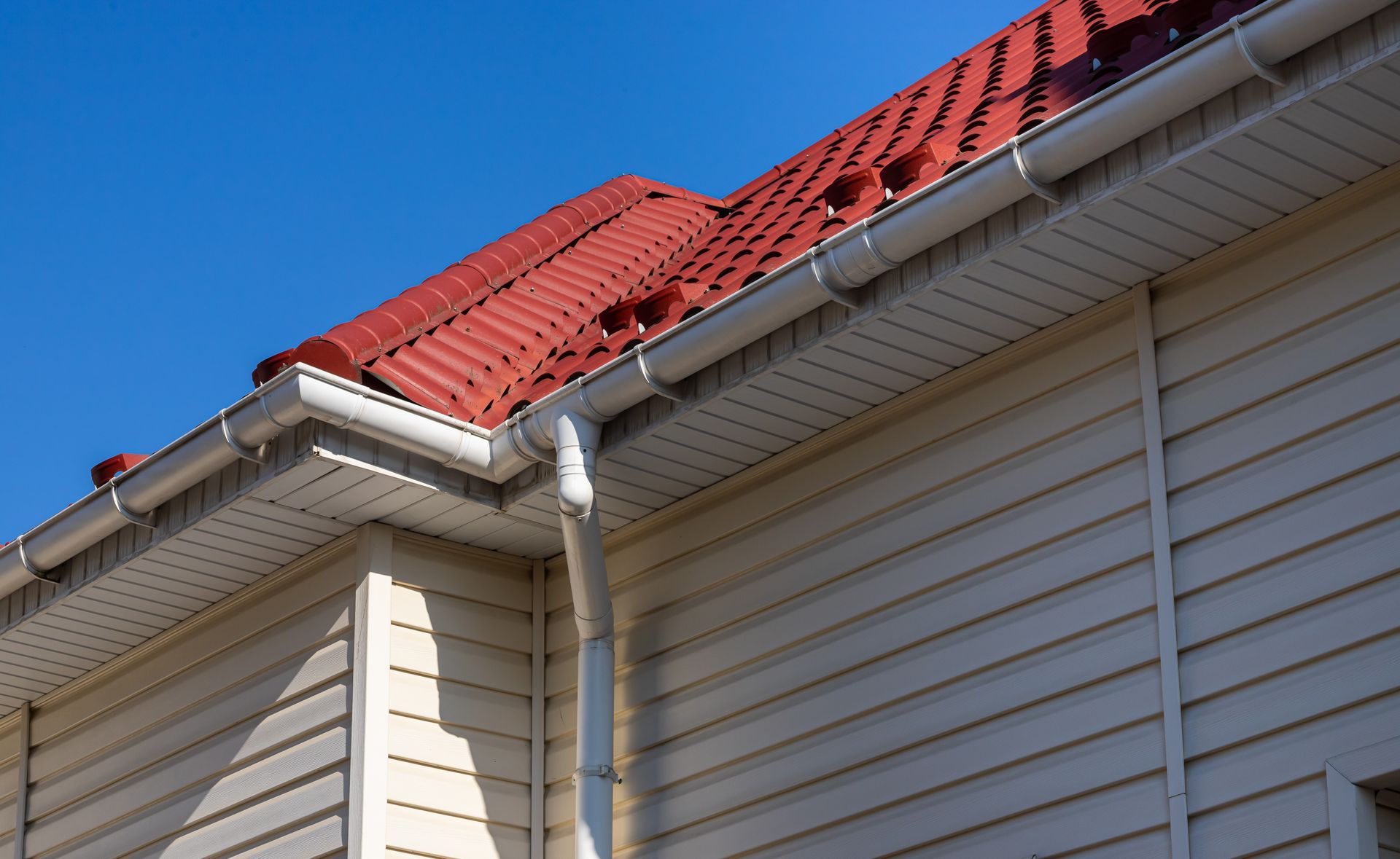 House corner with white planks siding and roof with gutter rain system and pipes installation.