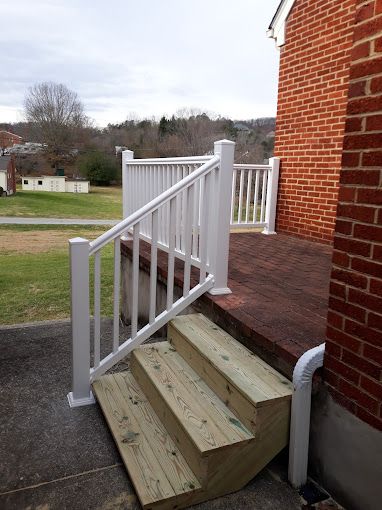 Wooden steps leading up to a deck with white railings next to a brick building.