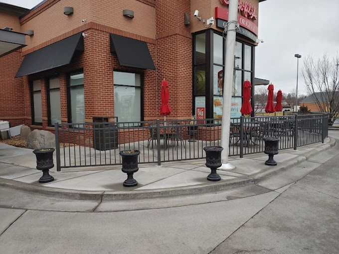 Exterior of Chick-fil-A with outdoor seating area, red umbrellas, and black metal railings, on a gray day.