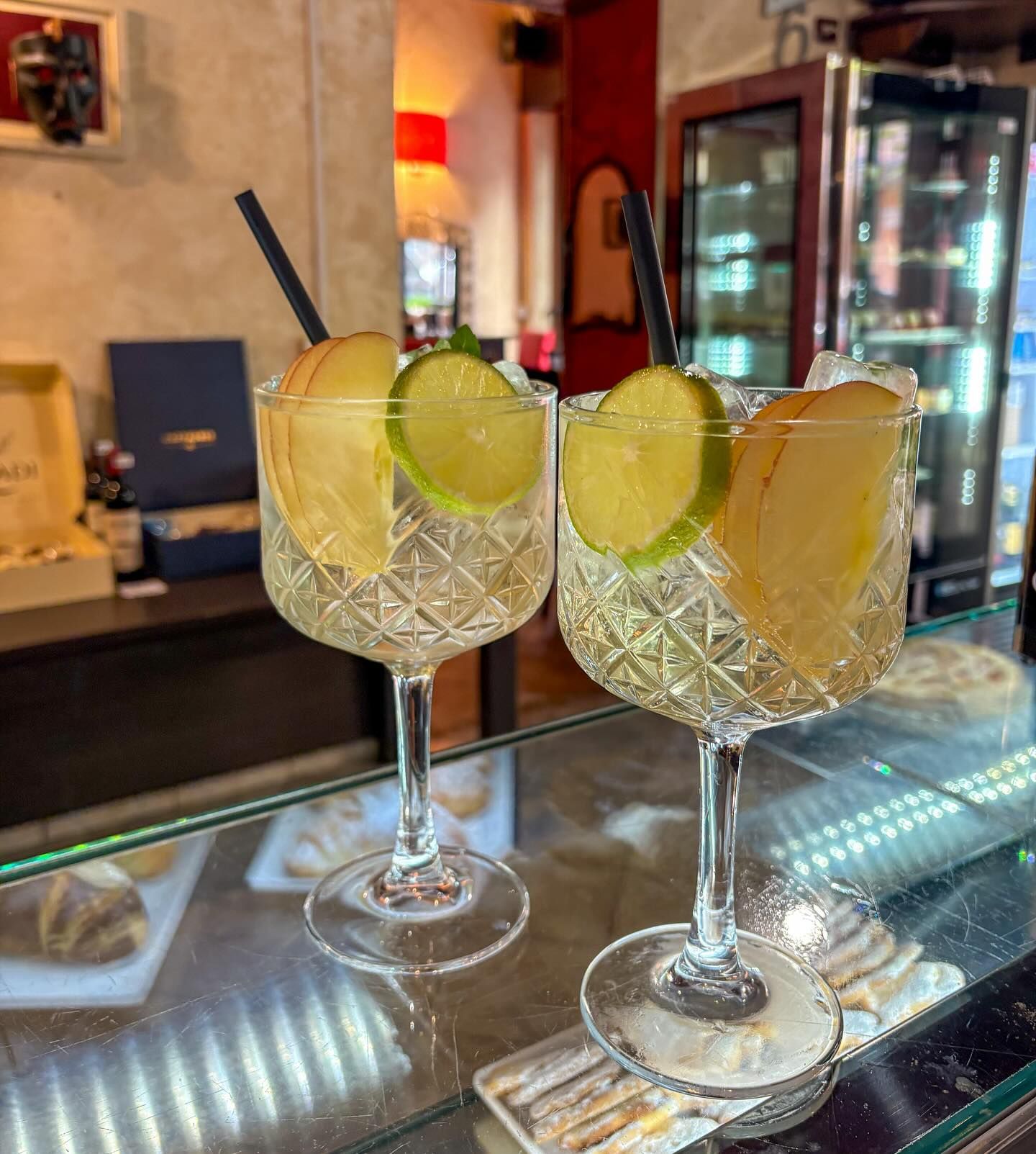 Due cocktail con guarnizioni di mela e lime, serviti su un bancone.