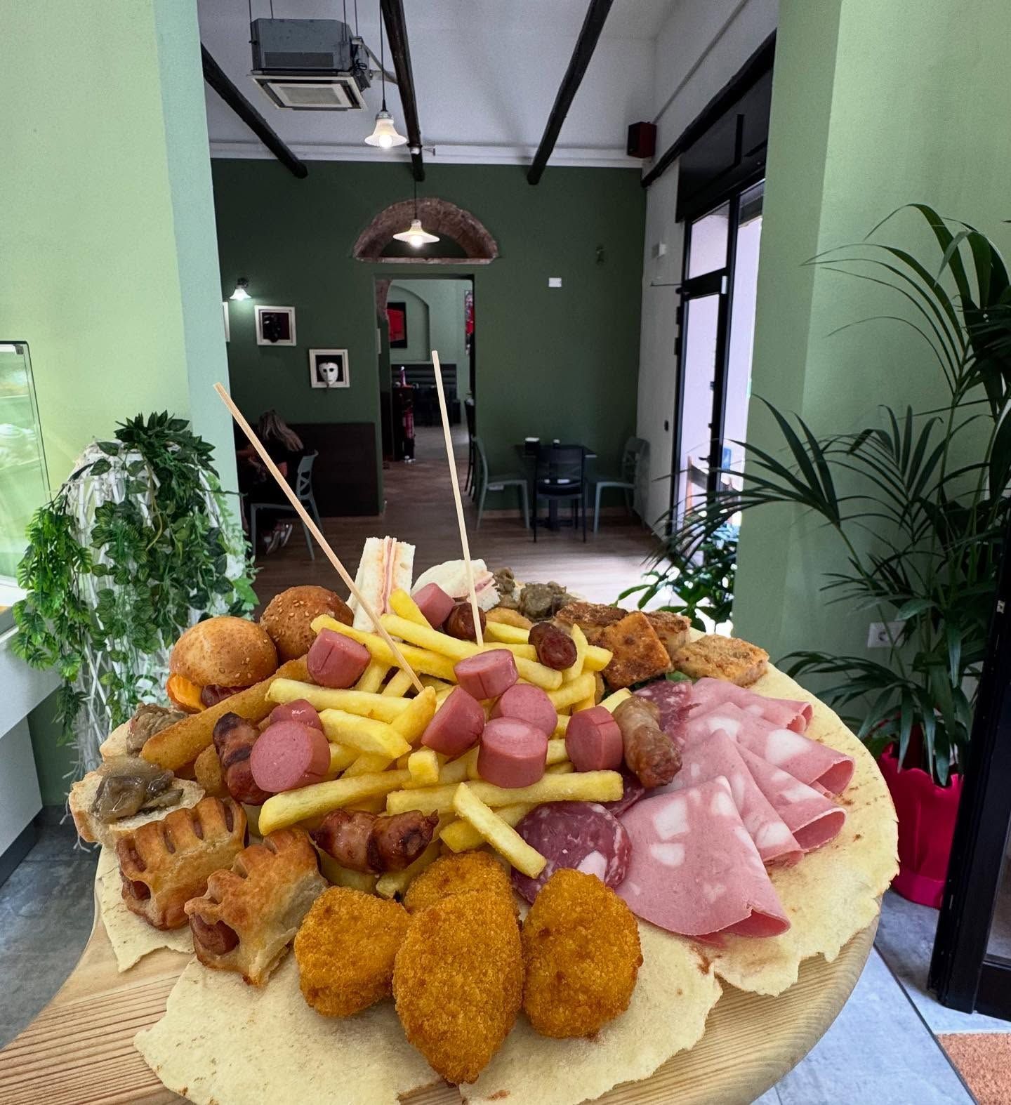 Un grande piatto con cibo fritto, salsicce, patatine fritte e affettati, servito al chiuso.