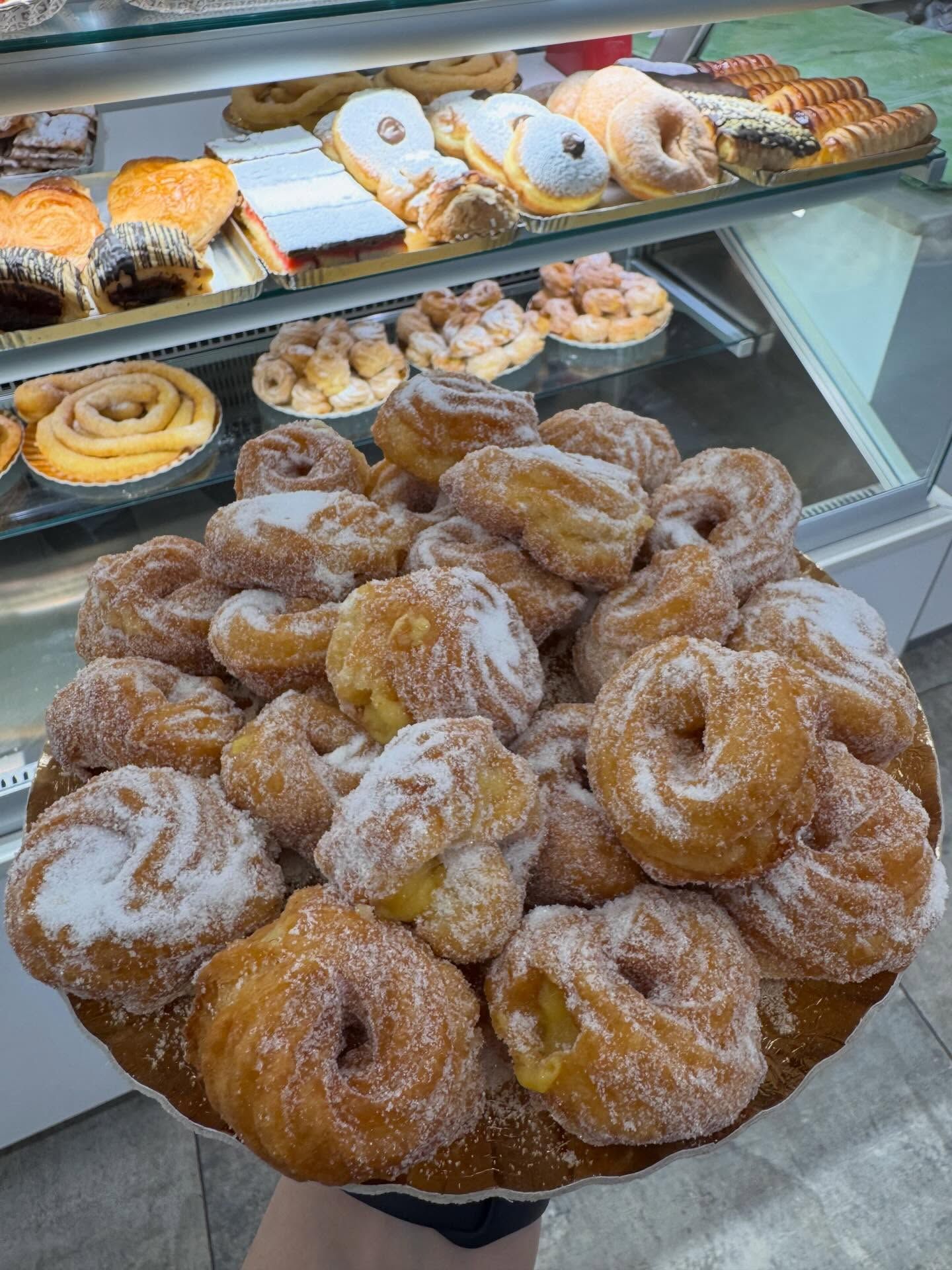 Vassoio di pasticcini zuccherati davanti a una vetrina di prodotti da forno.