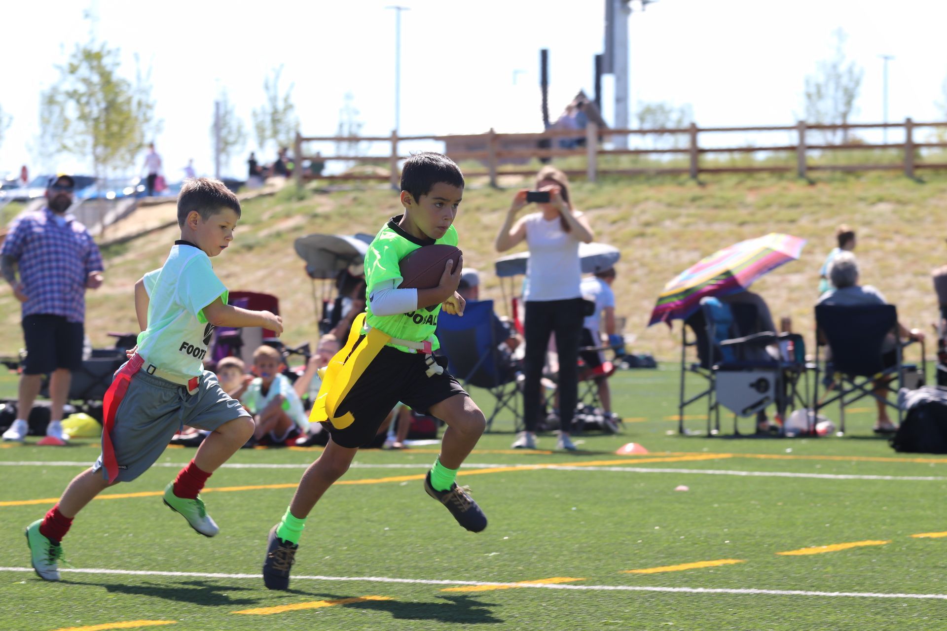 Two children playing flag football on a turf field.