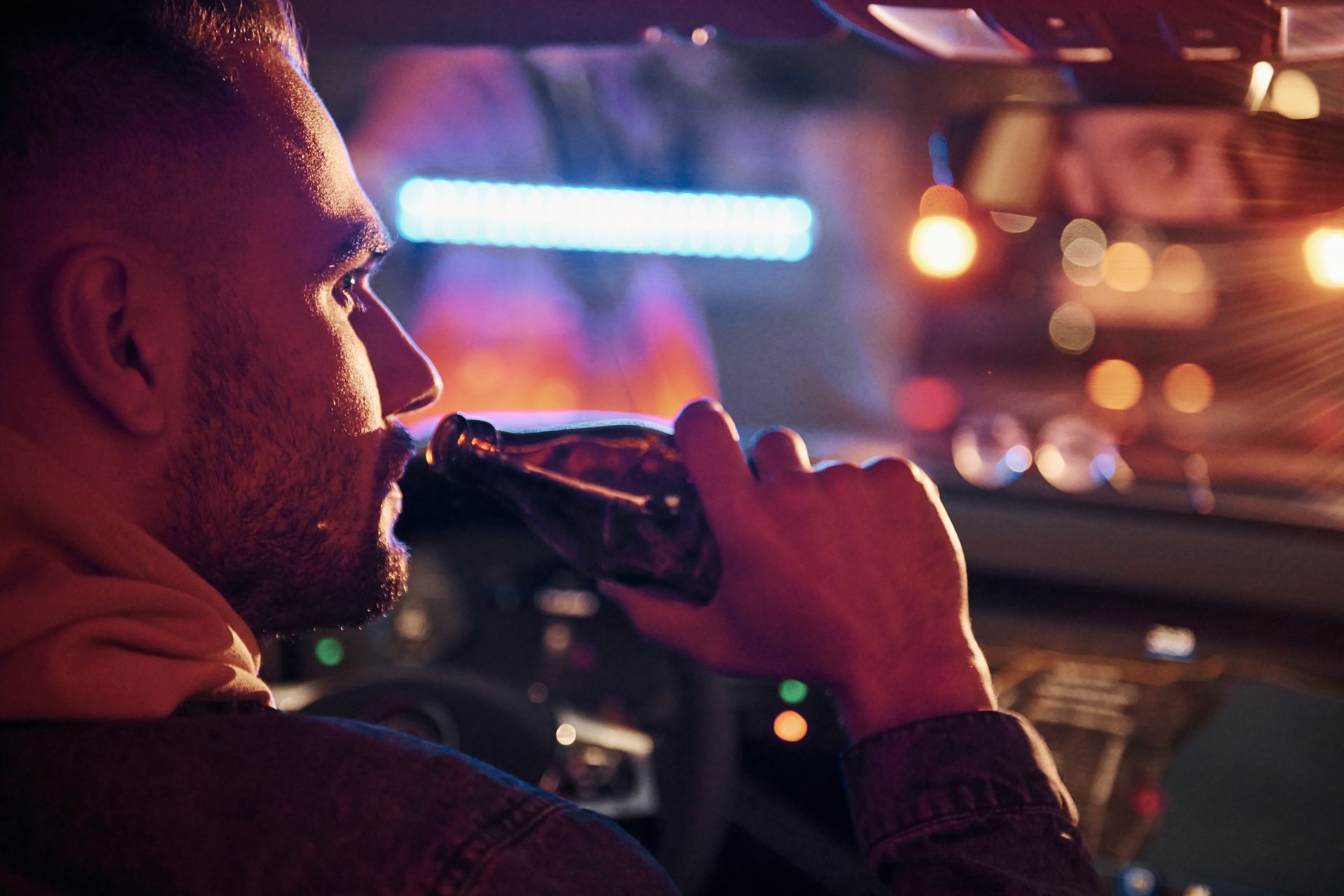 A man is drinking a beer while driving a car at night.