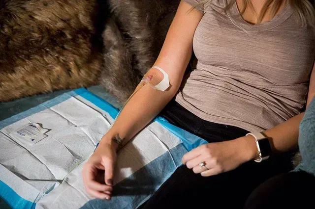 A woman is sitting on a couch with an iv in her arm.