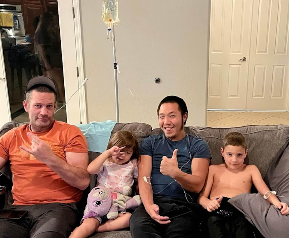 Three men and two children are sitting on a couch with an iv in their mouths.